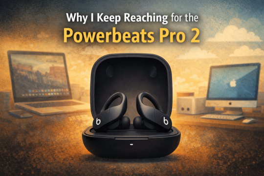 Powerbeats Pro 2 wireless earbuds in charging case on a desk with Apple computer setup in the background